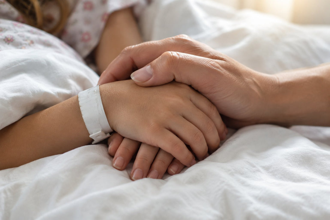 La main d'une mère posée sur celle de sa fille, qui porte encore un bracelet d'hôpital.