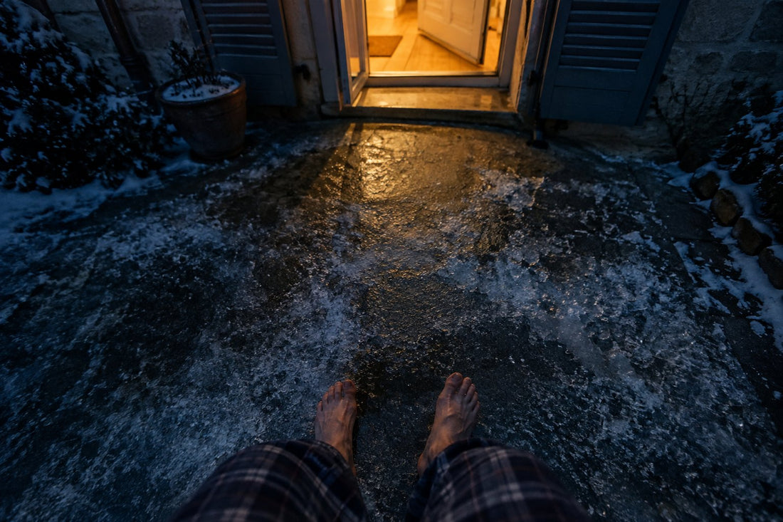 Des pieds nus sur une allée gelée, la nuit, devant la porte d'entrée ouverte.